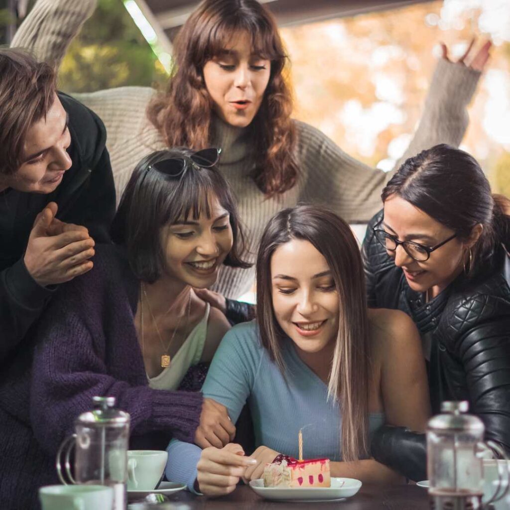 At a friend's birthday celebration, the guests pose for pictures while standing near the cake table,