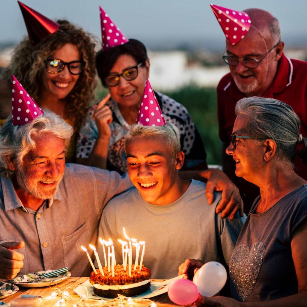 Group of cheerful elderly people having fun at their grandson's birthday party, wearing party hats, 